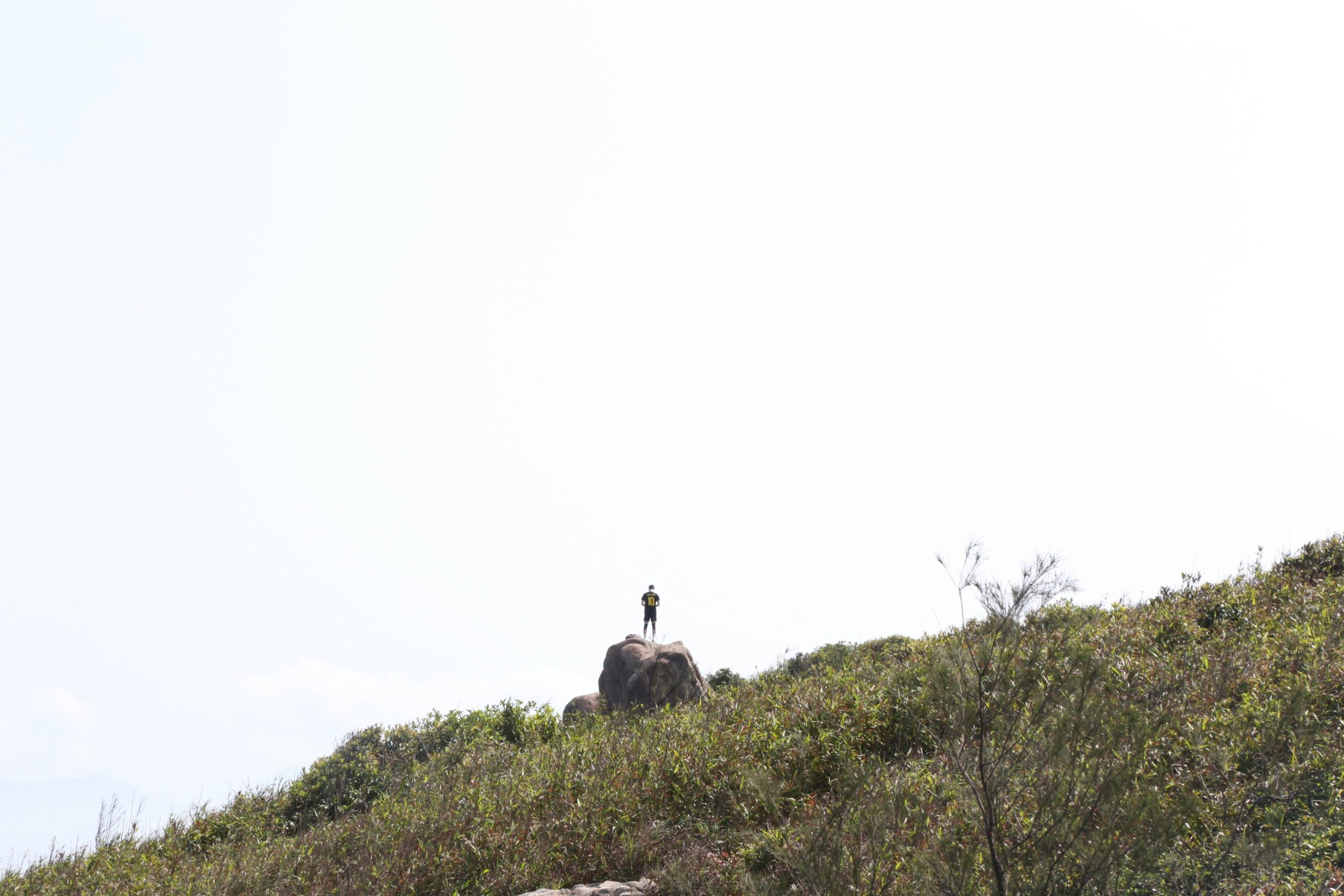 A hiker holding a DSLR camera while standing on a mountain peak.
