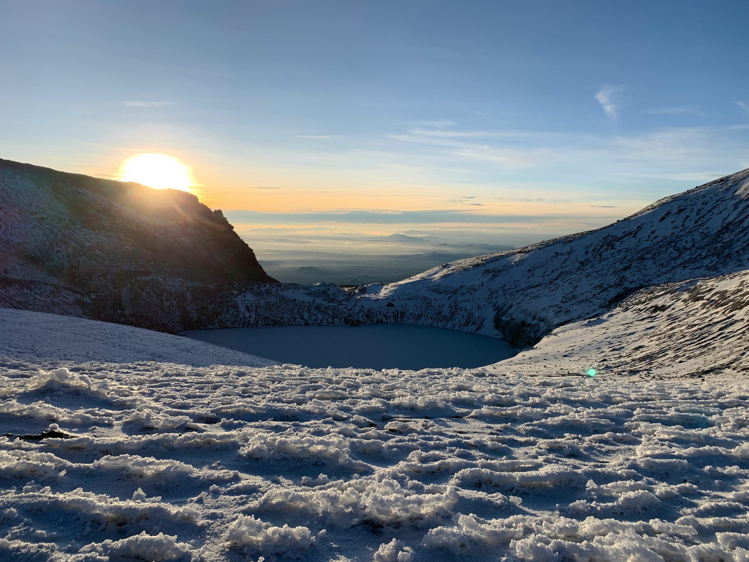 Rachel holding her Sony RX100 VII while standing atop snowy mountains with vibrant sunrise behind her